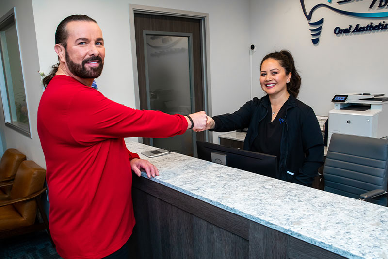 Patient and dental practice staff member smiling and shaking hands after dental implant procedure